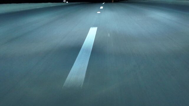 Low angle POV asphalt road with lane markings. Night