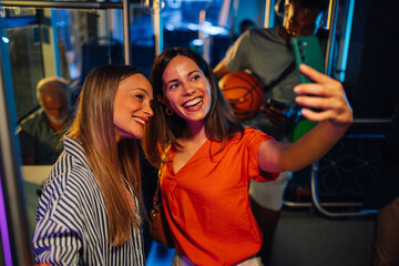 Two happy women taking selfie on night bus ride