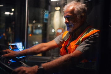 Senior bus driver steering vehicle at night, focused on road