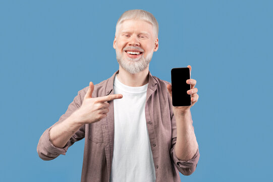 Check this app. Joyful albino guy holding cellphone and pointing finger at smartphone with black screen, studio background with free space. Mockup for mobile application or website - Powered by Adobe