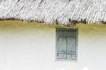Ancient Central European thatched-roof structure, likely made of stone or concrete, with weathered wooden window and contrasting textured walls