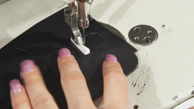 Special machine creates precise circular stitches on fabric. Person with glittery nails adjusts fabric to ensure great accuracy