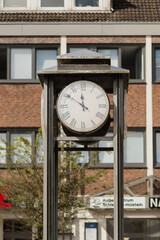 A classic style street clock with a white dial and Roman numerals in Germany, Preetz. The clock is mounted on a metal stand, which appears to be part of a lamp post or a separate structure