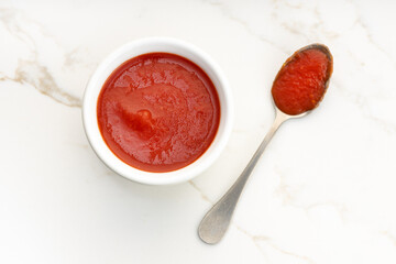 Fresh tomato sauce on bowl and spoon on white marble table