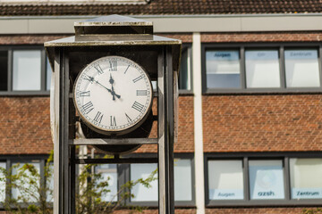 A classic style street clock with a white dial and Roman numerals in Germany, Preetz. The clock is mounted on a metal stand, which appears to be part of a lamp post or a separate structure