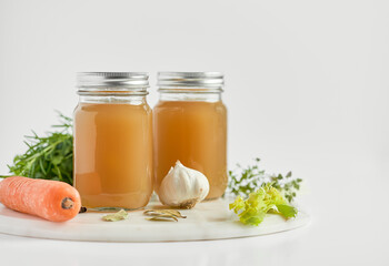 Jars of bone broth in white background with ingredients.
