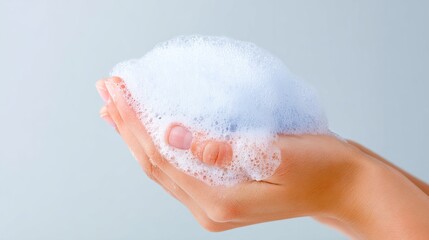Fototapeta premium Close-up of a hand holding a fluffy lather of soap bubbles against a soft gradient background, illustrating cleanliness and hygiene in personal care routines