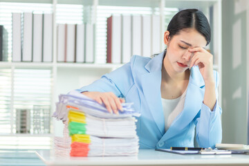Businesswoman stressed searching for documents to check accounts and analyze business plan from a large number of documents on her desk. Businesswoman stressed over a large number of documents