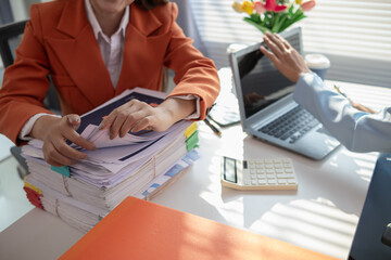 businesswoman and her secretary are helping search for documents examine large number investment documents piled on desk. businesswoman is having trouble finding large number documents piled on desk.