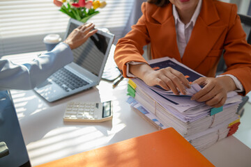 businesswoman and her secretary are helping search for documents examine large number investment documents piled on desk. businesswoman is having trouble finding large number documents piled on desk.