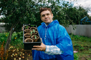 A farmer with a trendy hairstyle and stylish glasses looks at seedlings of cucumbers and tomatoes in peat pots. the gardener at the cottage is preparing to plant young plants in the garden.