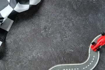 Fototapete Rund Formel 1 Checkered flag and formula 1 red toy race car on curved puzzle track over dark textured background.  © photoguns