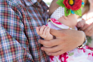 Close-up of a baby holding an adult’s hand, symbolizing love, tenderness, and family connection. The baby wears a floral outfit with a headband decorated with a bright red flower.