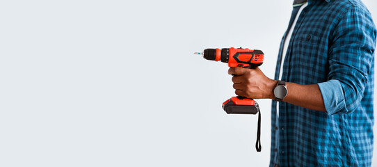 Naklejka premium Accessories for renovation apartment. Black man with smartwatch holding electric drill, ready to repair home furniture, standing over white background, side view, panorama with empty space, crop