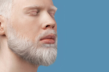 Obraz premium Calm bearded albino man with closed eyes resting against turquoise background. Extraordinary guy with white hair, eyelashes and brows. Panorama with empty space. Albinism, uncommon appearance concept