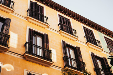 An old European building facade with windows and balconies in warm colors, bathed in sunlight. View of an old building facade featuring windows with black shutters and balconies. European city street.