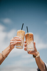 Two people are holding up two glasses of coffee, one of which has a straw in it © Reuben