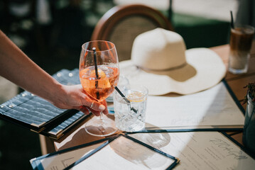 A person is holding a glass of wine and a straw in front of a table with a hat