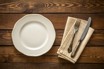Rustic table setting with an empty white plate and vintage silverware on a dark wood background. Top view of a place setting ready for a meal.
Generative Ai.