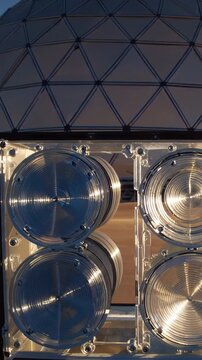 Vertical screen, multiple cherenkov telescope array reflectors rotate, reflecting the warm hues of the setting sun, showcasing advanced technology against a twilight sky