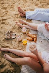 Three people are sitting on the beach, enjoying a meal and drinks