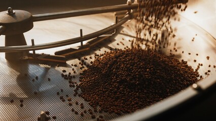 Stream of roasted coffee beans falling into perforated cooling tray under metal arms. Spreading across surface for airflow. Beginning cooling process. Locking in flavor and aroma. Finishing production