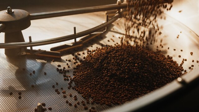 Stream of roasted coffee beans falling into perforated cooling tray under metal arms. Spreading across surface for airflow. Beginning cooling process. Locking in flavor and aroma. Finishing production