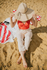 A woman is sitting on the beach wearing a red top and white pants