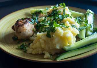 Homemade chicken drumstick with mashed potatoes, cucumber and parsley on a plate