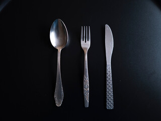 Spoon, fork and knife lying on a black background