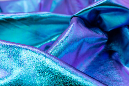 Shiny iridescent fabric with folds in turquoise, blue and violet tones, reflecting metallic light and creating a glossy abstract texture ideal for fashion, luxury, design and modern art concepts. - Powered by Adobe