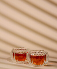 Two elegant glass cups filled with black tea placed on a soft surface, with hard shadows from blinds that create a warm and inviting atmosphere in a minimalist setting. Tea time, breakfast