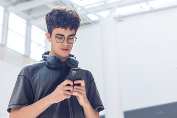 Smiling teenager with headphones using smartphone in shopping mall, young man listening to music, texting, chatting online, modern digital lifestyle, social media and youth technology concept.