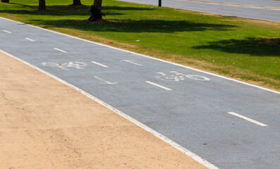Obraz premium Bicycle path marked with lane lines for cyclists running parallel to a grassy area, providing a safe space for biking and outdoor activities in sunny weather.