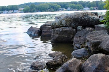 Relaxing Lakeside View Featuring Smooth Rocks and Gentle Water in the Backdrop of Lush Greenery and Serene Nature, Perfect for Tranquil Moments
