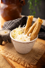 Flautas Ahogadas (Drowned Flautas) Golden tacos made with fried corn tortillas, filled with chicken or beef, and served in a glass or cup containing salsa or broth, lettuce, sour cream, and cheese.