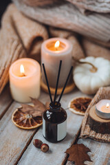 Concept of house decor, apartment seasonal fragrance. Thanksgiving. Autumn mood, cozy fall home atmosphere. Aroma diffuser, pumpkins, knitted warm sweaters, burning candles, dry leaves on wooden table