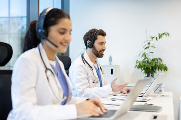 Medical professionals providing telehealth assistance using laptops and headsets in modern office
