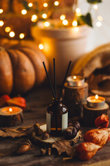 Autumn cozy mood composition with burning candles. Aroma stick reed diffuser, pumpkin on wooden table, knitted warm plaid. Fall hygge home decor, aromatherapy. Relaxed atmosphere in the apartment