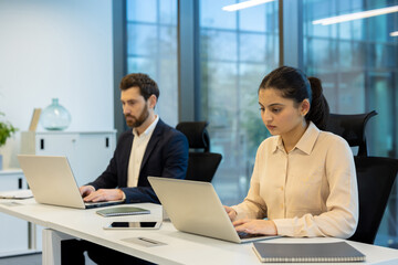Two professionals working on laptops in a bright modern office setting