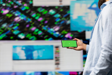 Young guy looks at green screen on phone as a user interface, checking online presence on social platforms. Male Influencer working on creativity and online engagement in a digital world.