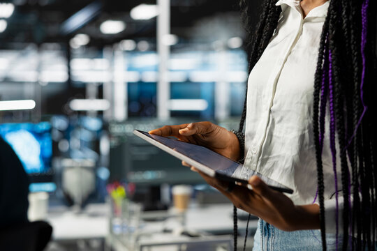 Close up of data center engineer using tablet, deploying and maintaining server and network hardware. Server hub employee using device to manage large scale IT infrastructure