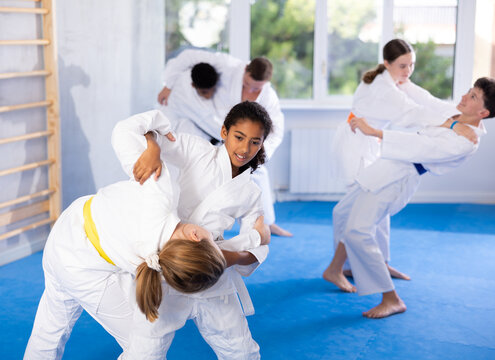 Two girls in kimonos train judo techniques in group in studio..