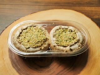 Two stuffed mushrooms in a plastic package on wooden background. Fine meal made of natural ingredients. Agriculture and farming, Food industry