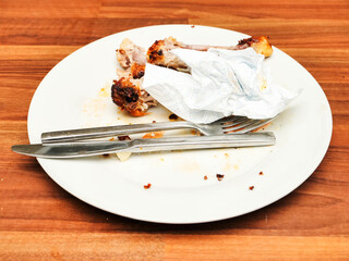 Dirty plate with chicken drumsticks bones and fork and knife on a wooden table. All food is eating. Good appetite concept. Food consumption.