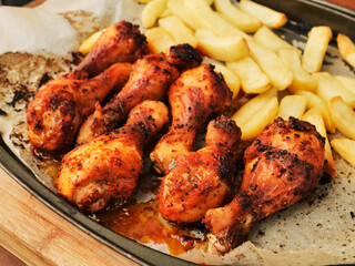 Metal tray with cooked marinated chicken drumsticks and chips. Simple tasty food. Small dinner for a few people. Drumsticks have strong red color and spice herb coating.