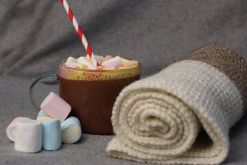 Hot cocoa with marshmallows and red-and-white straw next to cozy knitted plaid