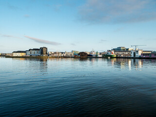 Naklejka premium Swans in river Corrib on the way to the ocean. Scene in Galway city, Ireland. Nimmos Pier area, high tide, The Long walk area in the background. Popular travel area.