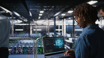 System administrators in data center monitoring AI LLM visualization. African american server farm coworkers overseeing rigs powering machine learning processes,