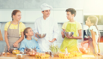 Group of teenagers and friendly chef cook cooking in kitchen. Learn to beat raw eggs